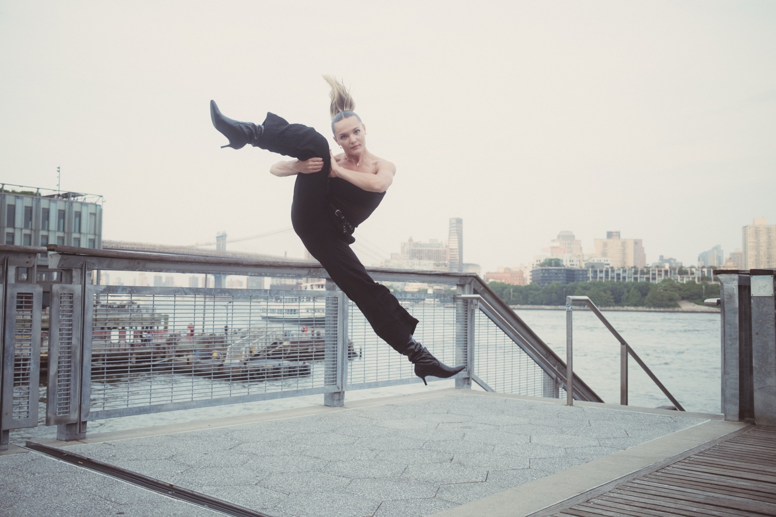 Dancer posing on a waterfront railing with city skyline