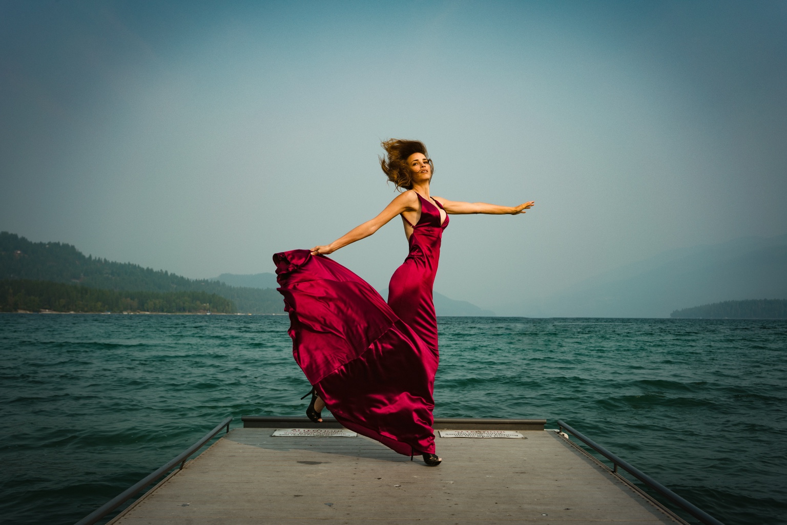 Model in a red dress standing on a dock over water